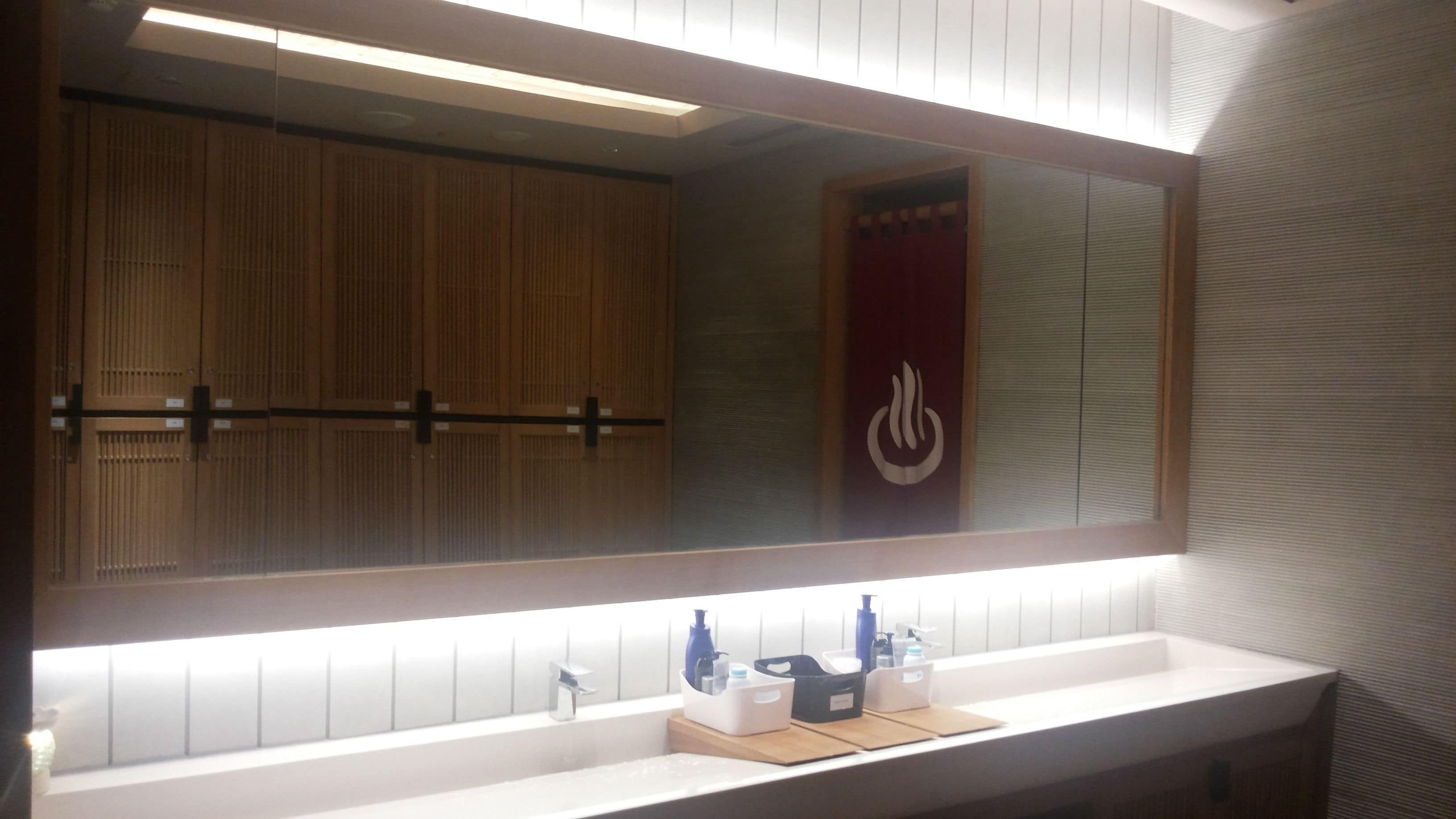 Une salle de bain avec un grand miroir, des meubles en bois, un lavabo blanc et un porte-serviettes.