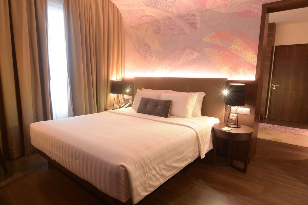 A hotel room with a large bed, two bedside lamps, a nightstand, a door, and a patterned wall.