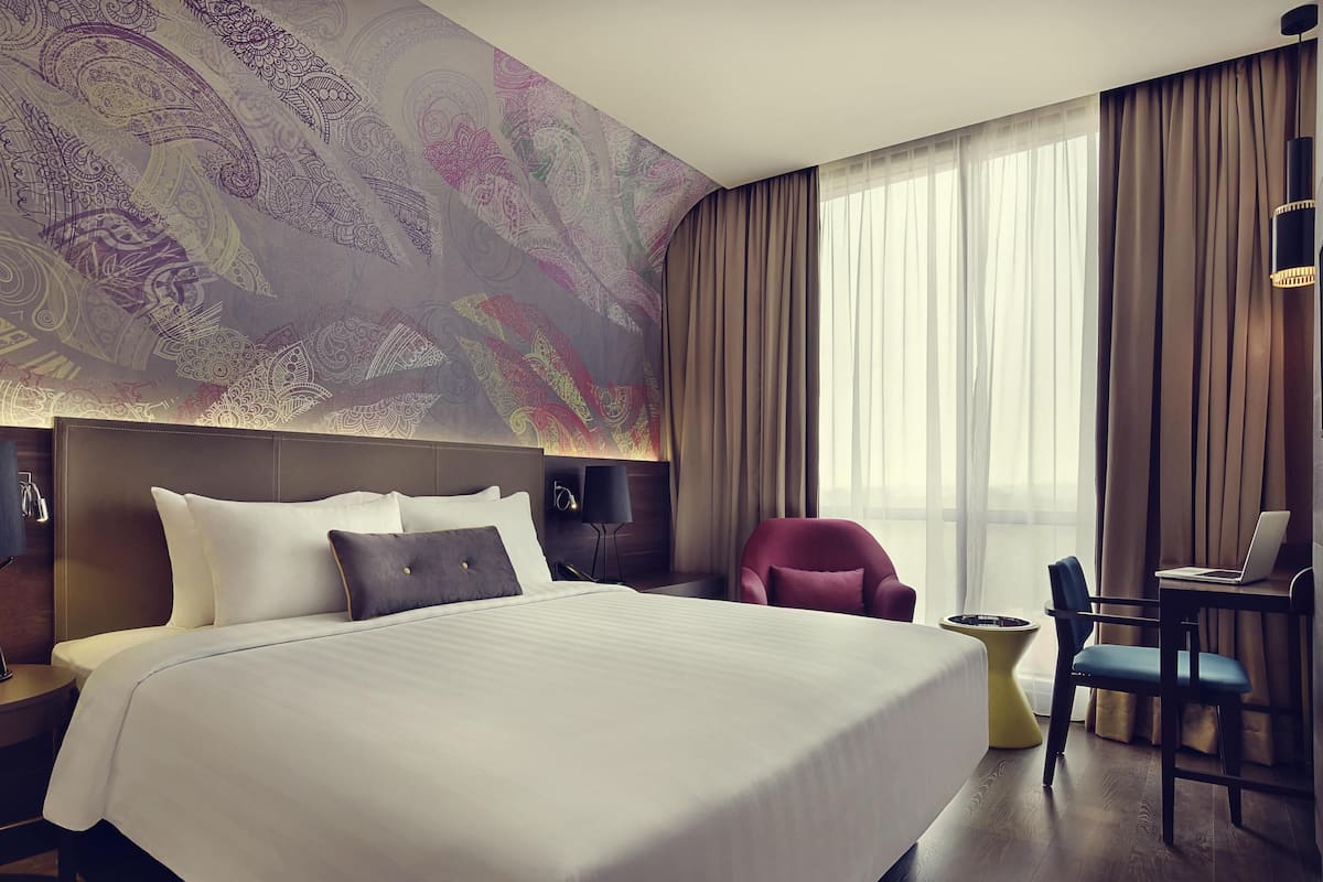 A hotel room with a large bed, a desk with a laptop, a chair, and a decorative wall.