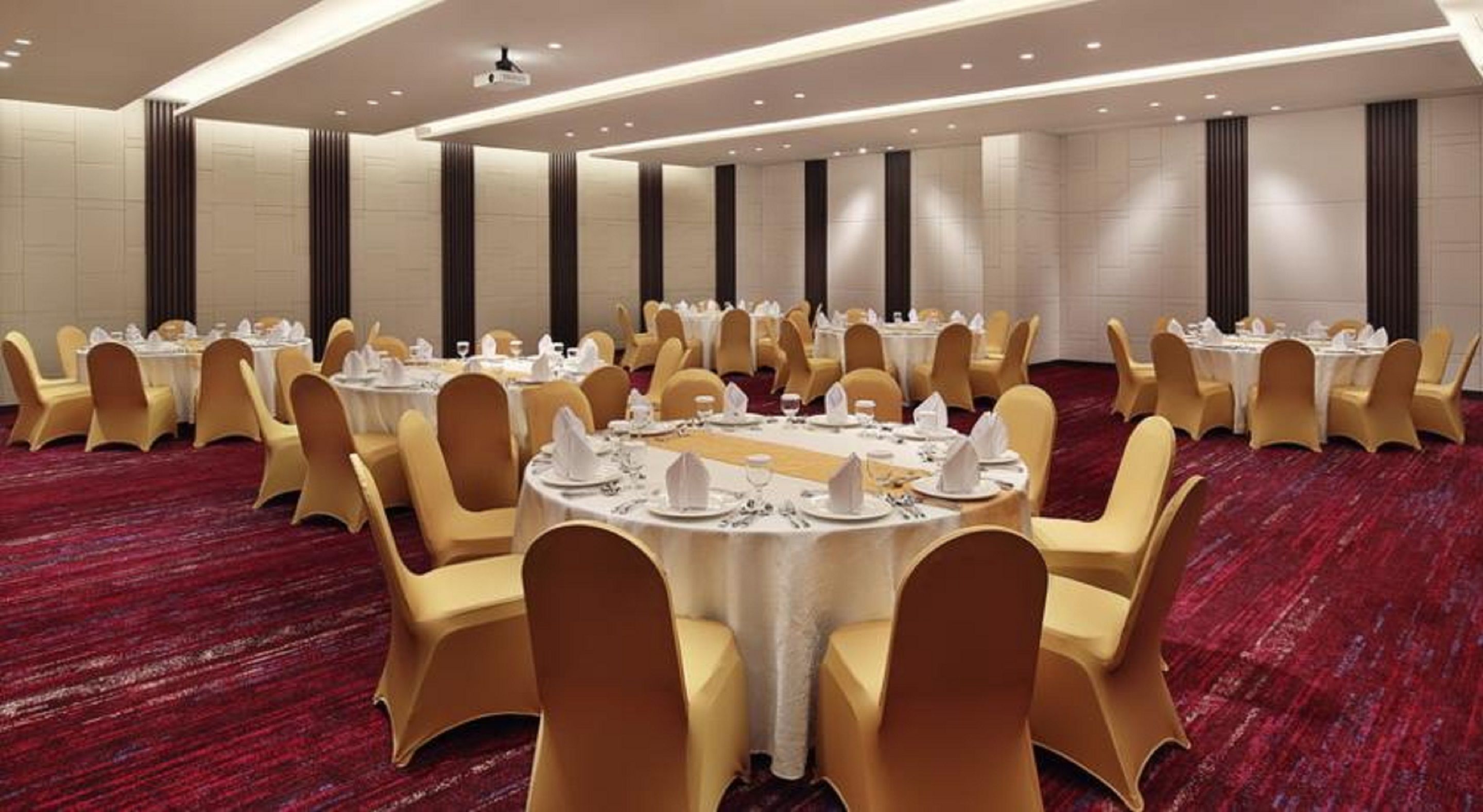 Un salón de banquetes con mesas redondas, sillas amarillas y una alfombra roja.