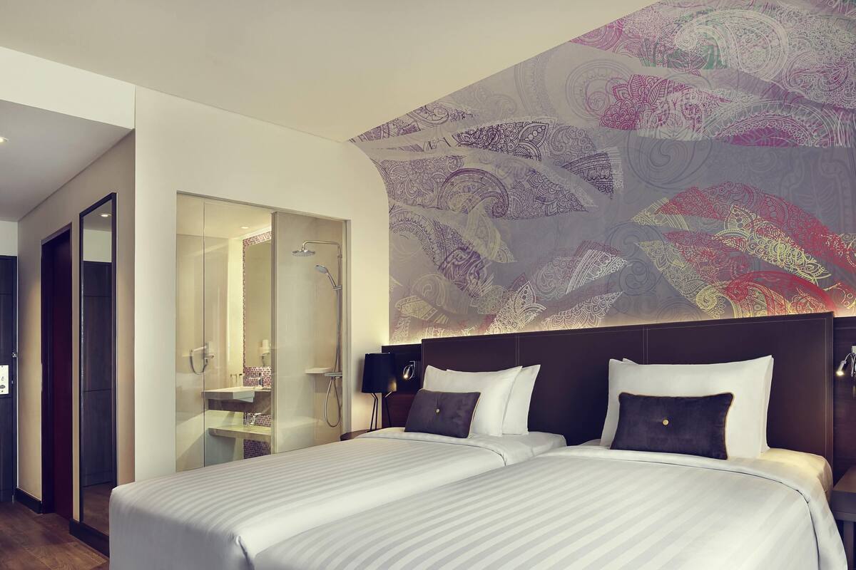 A hotel room with two beds, a large mirror, a shower, and a decorative wall.