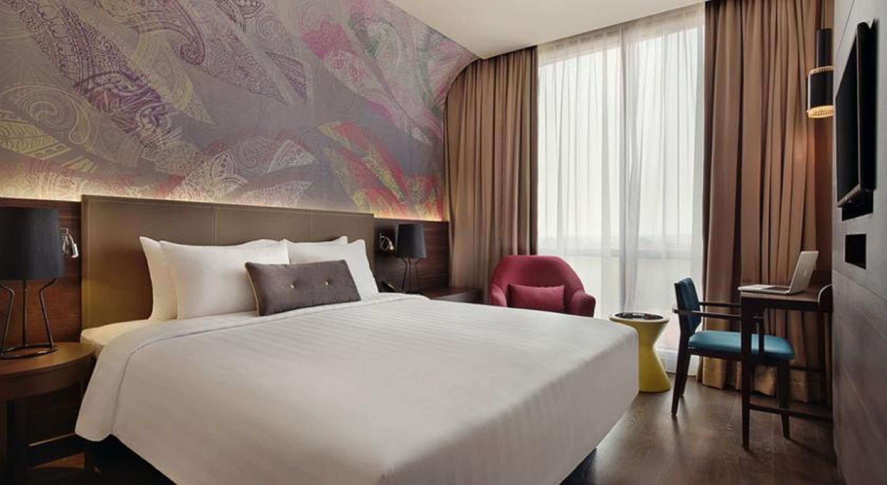 Une chambre d’hôtel avec un grand lit, un bureau avec un ordinateur portable, une chaise rouge et une petite table d’appoint jaune.