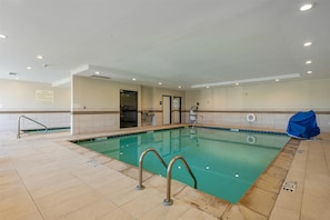 An indoor swimming pool with clear water, tiled floor, and metal handrails.