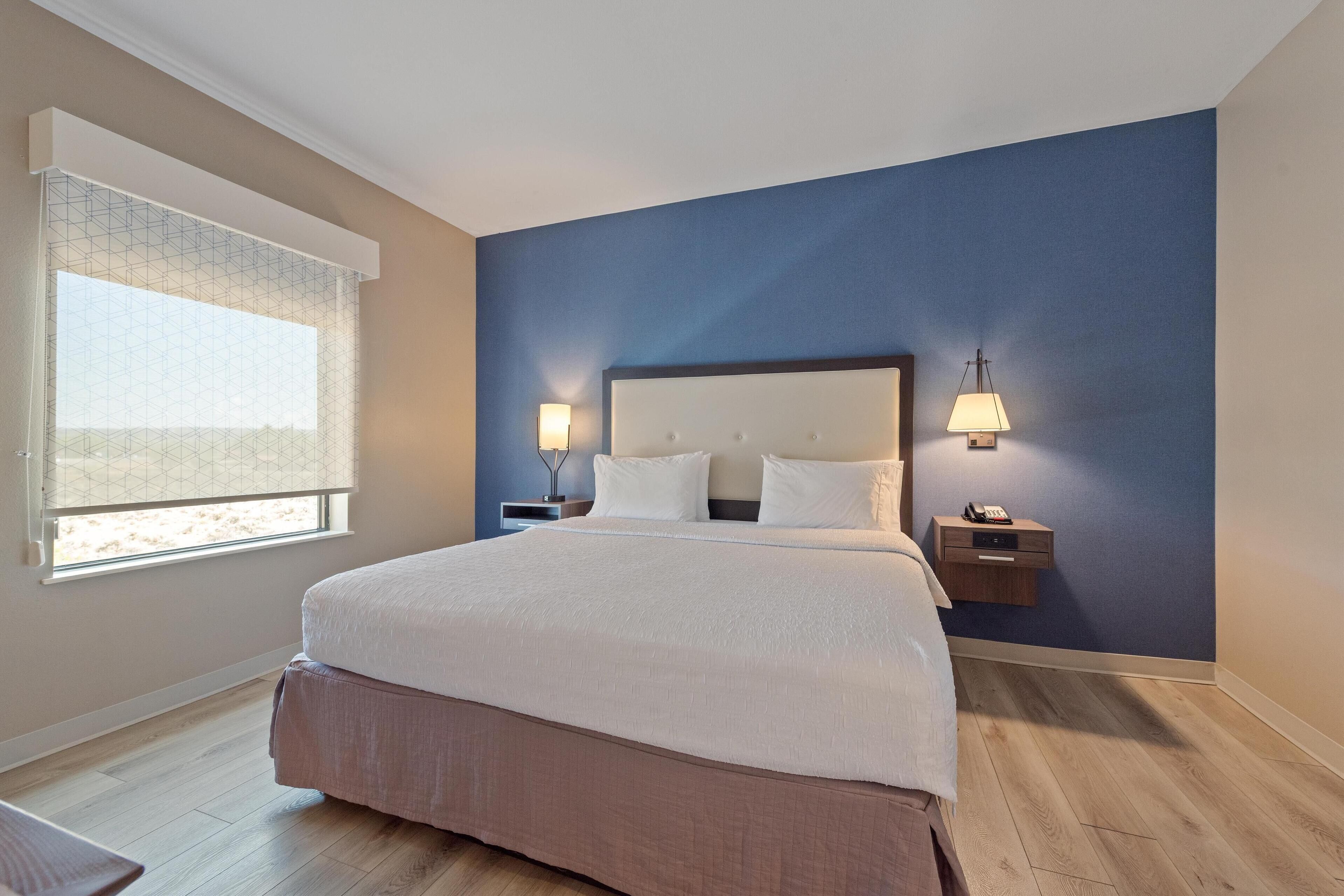 A neatly arranged bedroom with a large bed, two bedside tables, and a window with blinds.