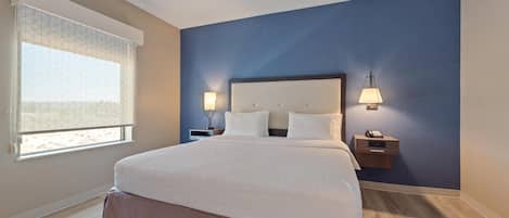 Un dormitorio ordenado con una cama grande, dos mesitas de noche y un ventanal con persianas.