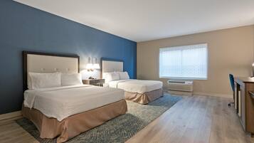 A hotel room with two beds, a desk, a chair, a window with blinds, and a radiator.