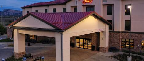 A Hampton Inn hotel with a covered entrance, a 15' clearance sign, and a parking area with benches.