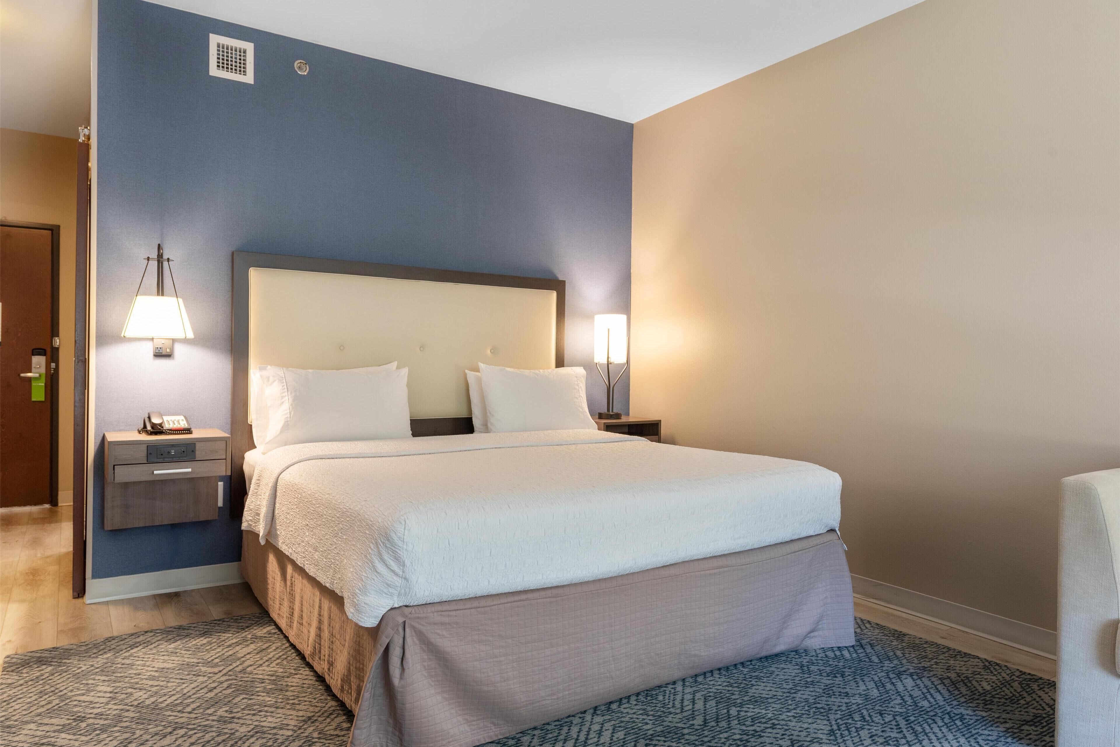 Habitación de hotel con una cama grande, dos mesitas de noche con lámparas, una mesita auxiliar y una alfombra estampada.