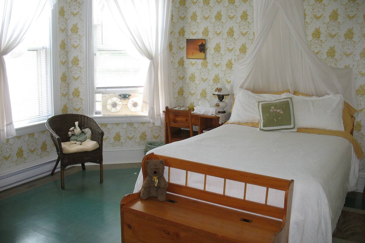 Een slaapkamer met een bed, een stoel, een nachtkastje, een lamp en een teddybeer.