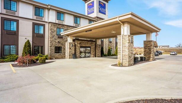 A Sleep Inn & Suites building with a covered entrance, stone facade, and a flag. - Sleep Inn & Suites Hannibal West (Hannibal)
