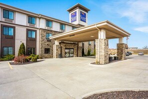 A Sleep Inn & Suites building with a covered entrance, stone facade, and a flag. - Sleep Inn & Suites Hannibal West (Hannibal)