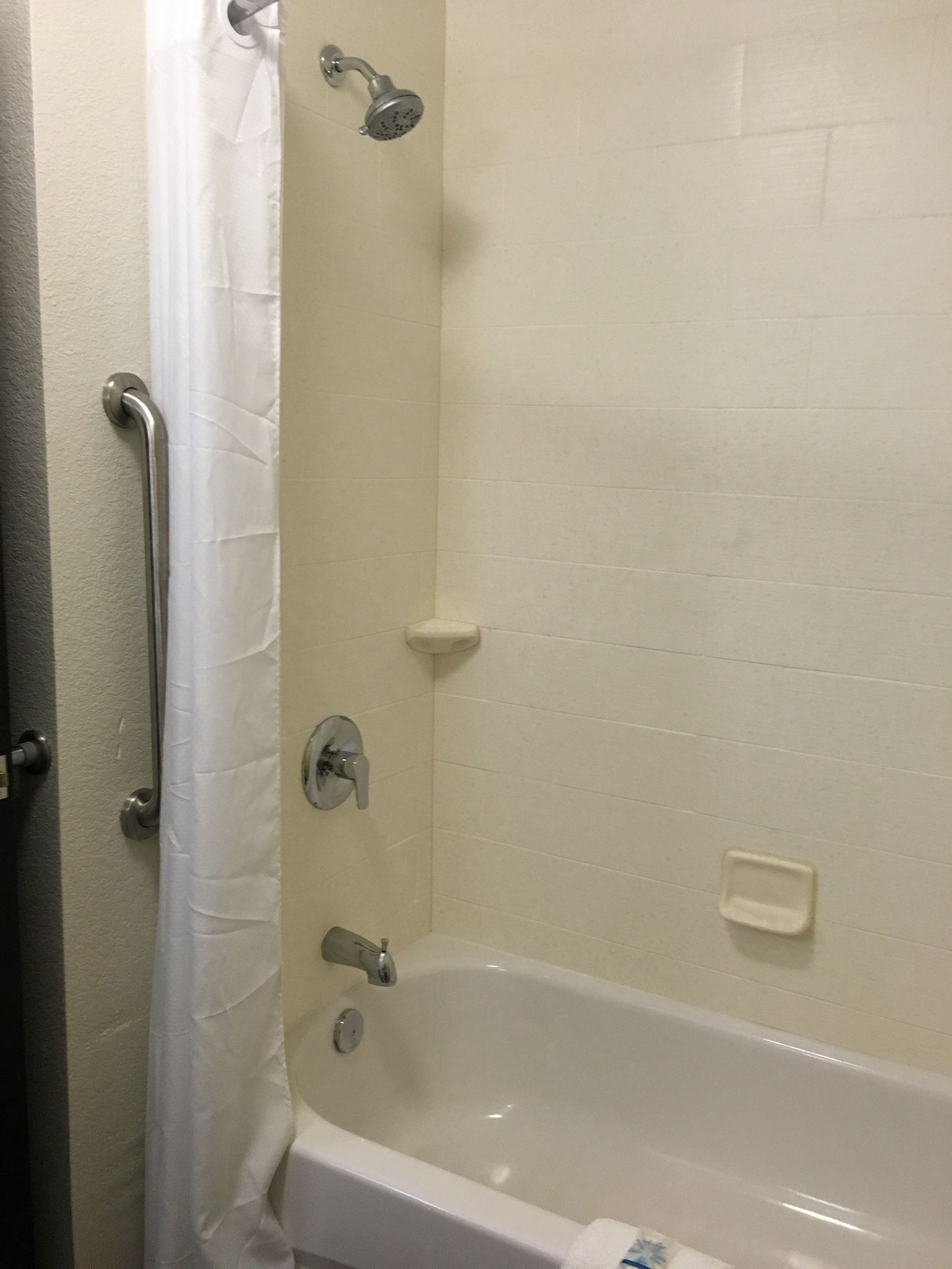 A bathroom with a bathtub, a shower head, a handrail, and a soap dish.