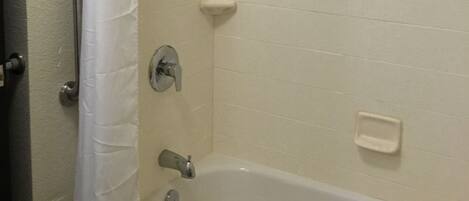 A bathroom with a bathtub, a shower head, a handrail, and a soap dish.