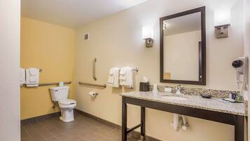 Une salle de bain équipée de toilettes, de barres d’appui, d’un lavabo, d’un miroir et de serviettes.
