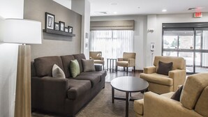 A modern lobby with a brown sofa, beige armchairs, a round table, and a floor lamp. - Sleep Inn & Suites Hannibal West (Hannibal)