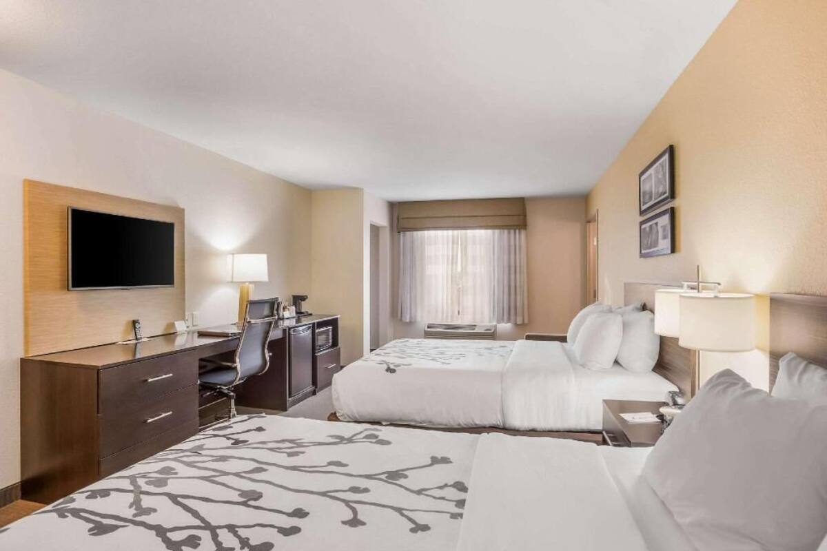 A hotel room with two beds, a desk, a TV, and a window with curtains.