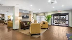 A lobby with a reception desk, a seating area with sofas and armchairs, a large potted plant, and a door leading outside. - Sleep Inn & Suites Hannibal West (Hannibal)
