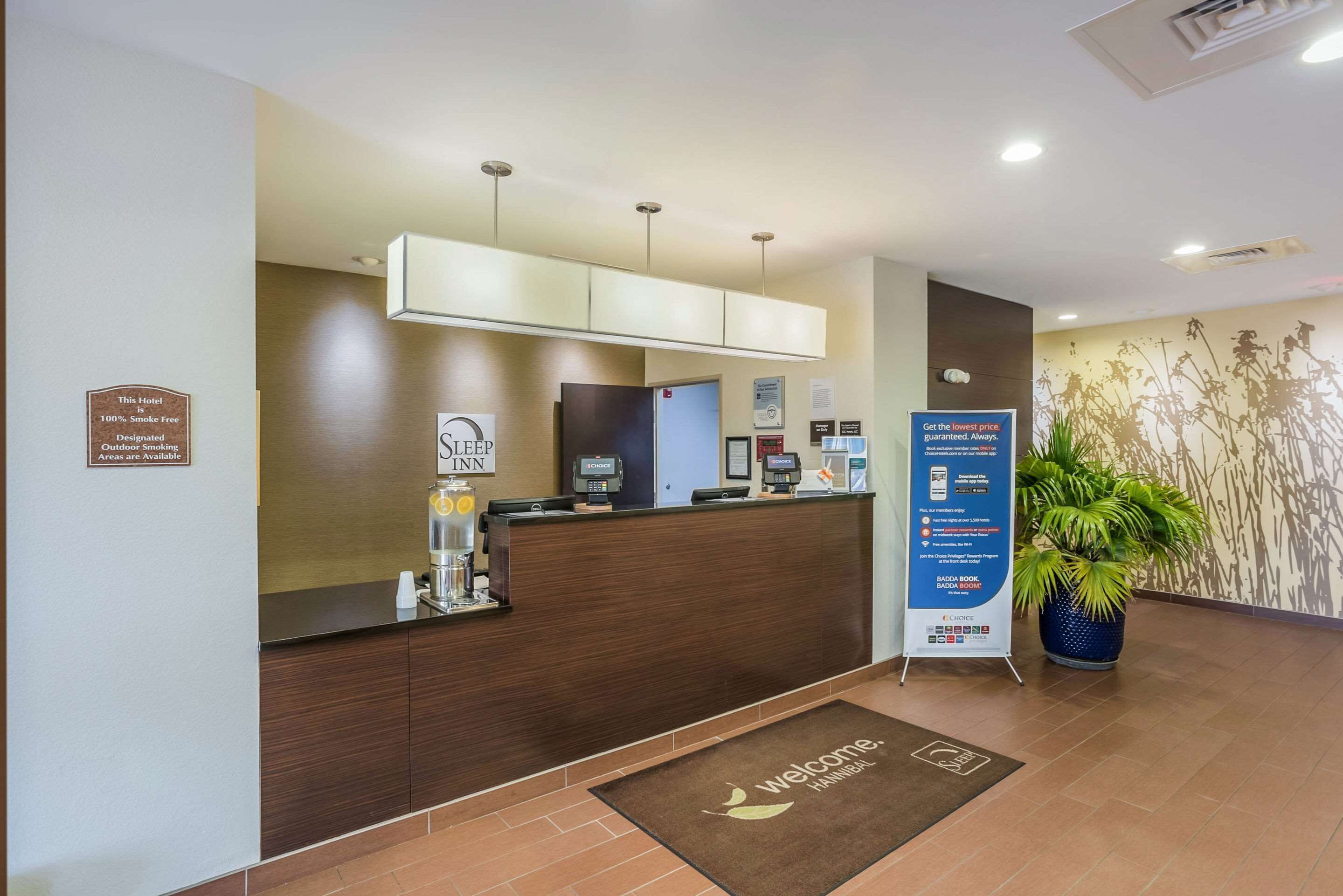 A hotel reception area with a wooden reception desk, a digital screen, and a welcome mat.