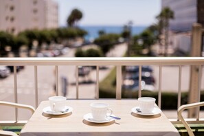 A balcony with two white cups on saucers, a spoon, and a view of the sea and buildings in the background. - Vistamar I - MC Apartaments Ibiza (Ibiza Town)
