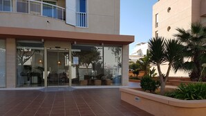 A building with a glass entrance, outdoor seating area, and steps leading up to the entrance. - Vistamar I - MC Apartaments Ibiza (Ibiza Town)