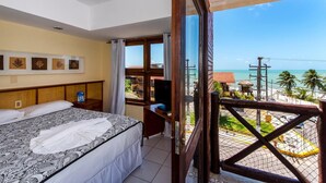 Habitación de hotel con cama, escritorio, televisor y balcón con vistas a la playa y al océano.