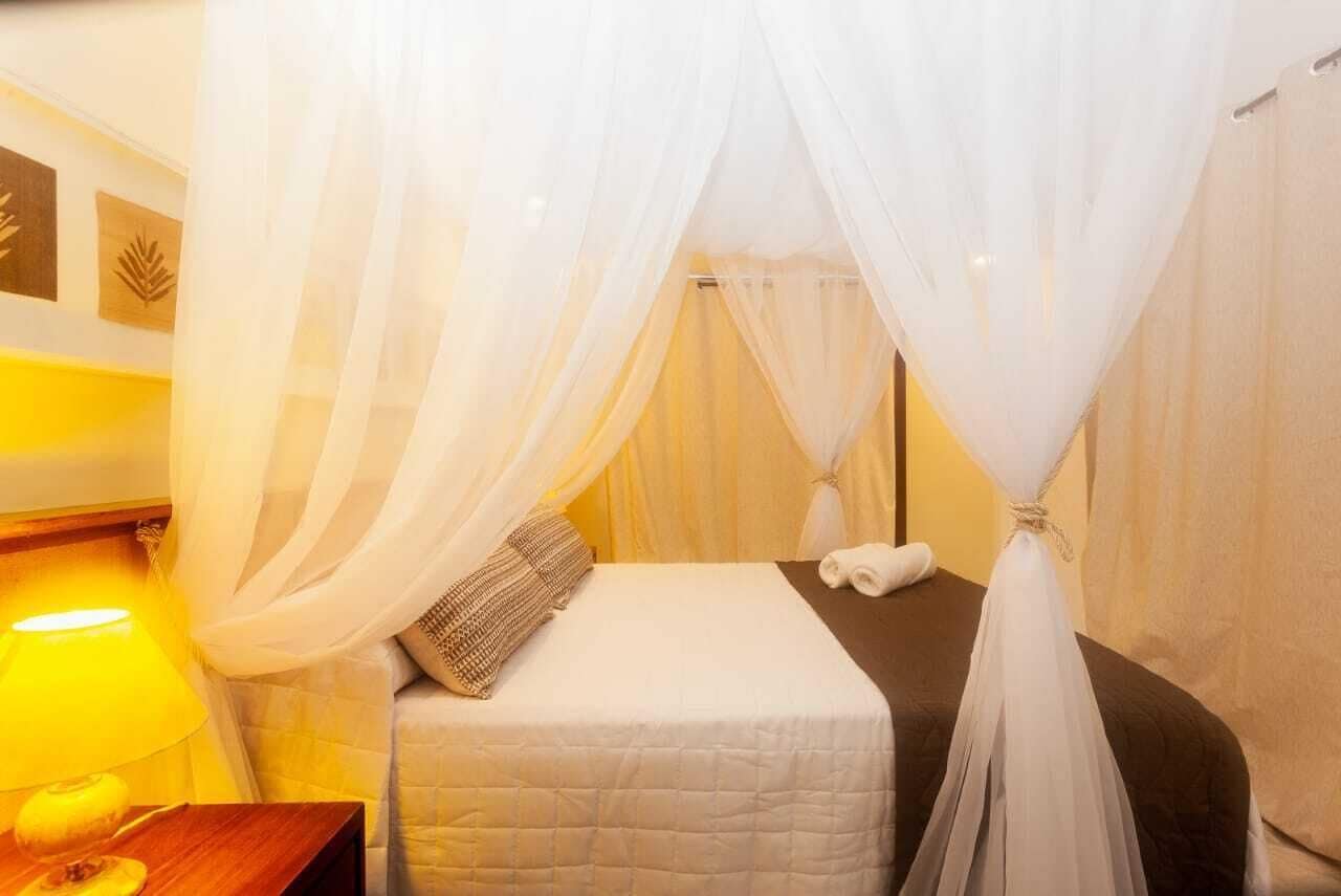 Una habitación de hotel con una cama, una mesita de noche, una lámpara y cortinas traslúcidas.