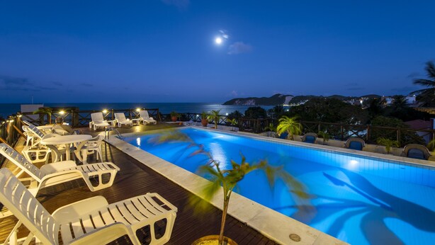 Un área junto a la piscina con sillones de descanso y una pequeña alberca, rodeada de palmeras y vista al mar.