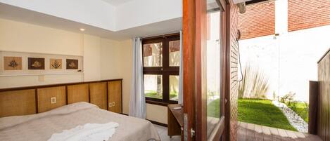A hotel room with a bed, a desk, and a view of a garden through a sliding door.