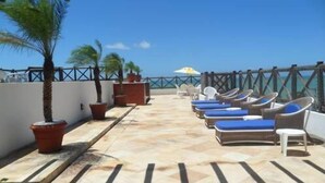 Terraza con sillones de descanso y plantas en macetas, con vista a un cielo azul despejado.