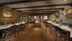 A restaurant with brick walls, wooden beams, and multiple dining tables with chairs. - Landgut Ramshof (Willich)
