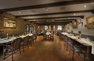 Un restaurante con paredes de ladrillo, vigas de madera y varias mesas con sillas.