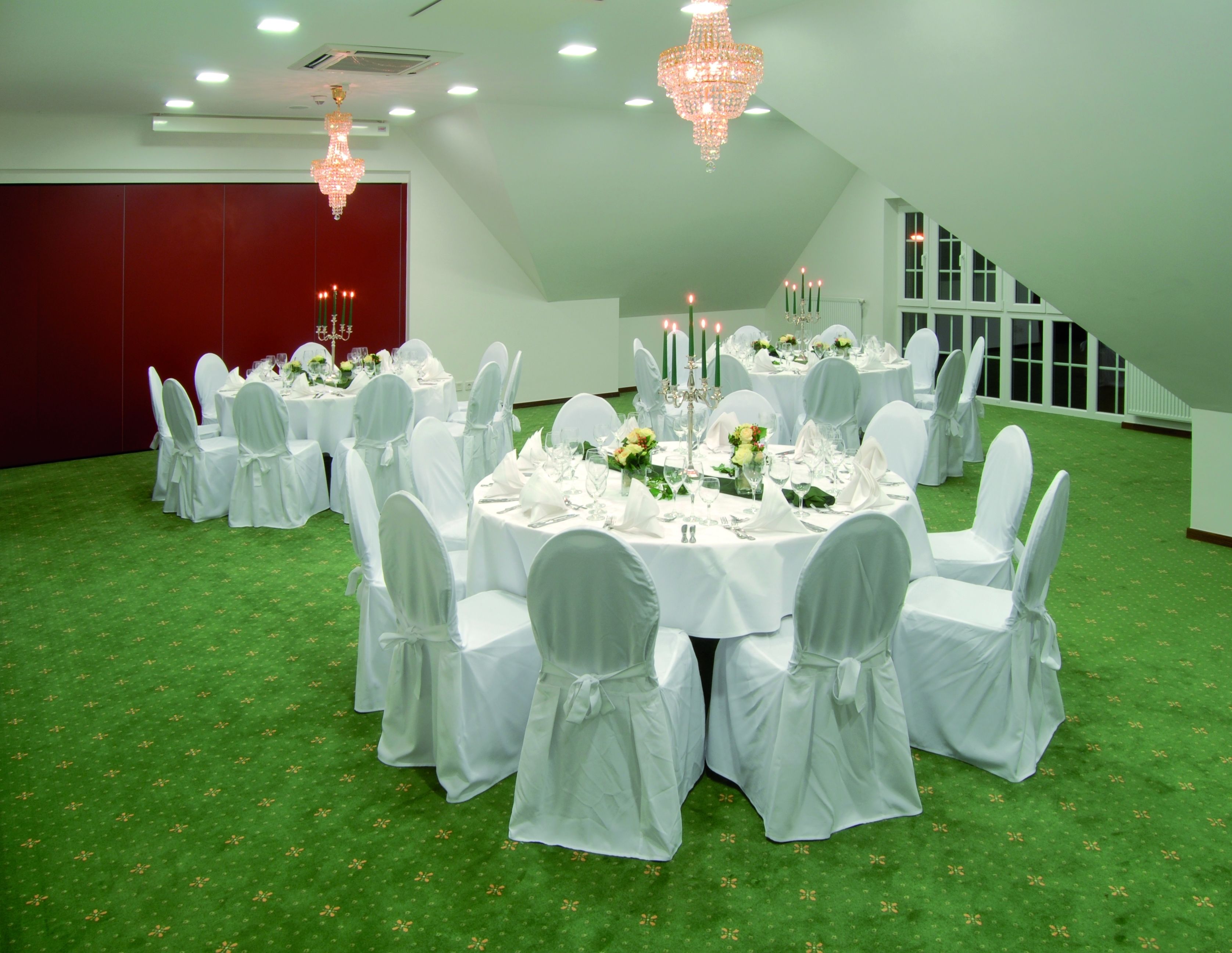 A banquet hall with round tables, white chairs, and chandeliers.