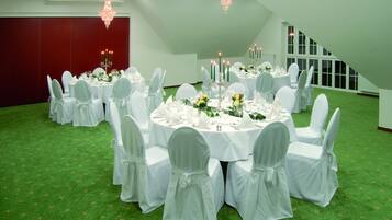 A banquet hall with round tables, white chairs, and chandeliers.