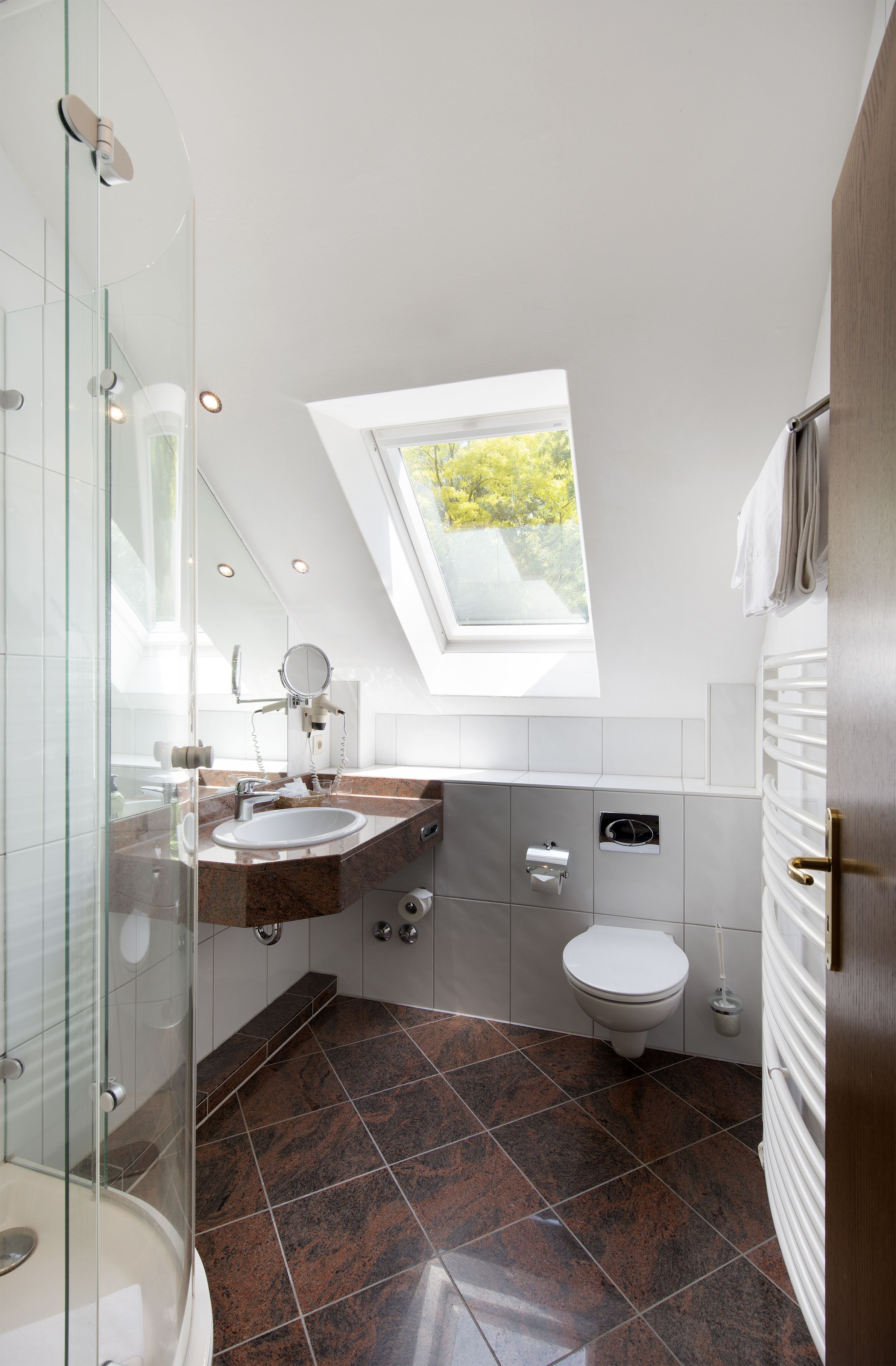 Un baño moderno con tragaluz, cabina de ducha de vidrio, lavamanos blanco y retrete.
