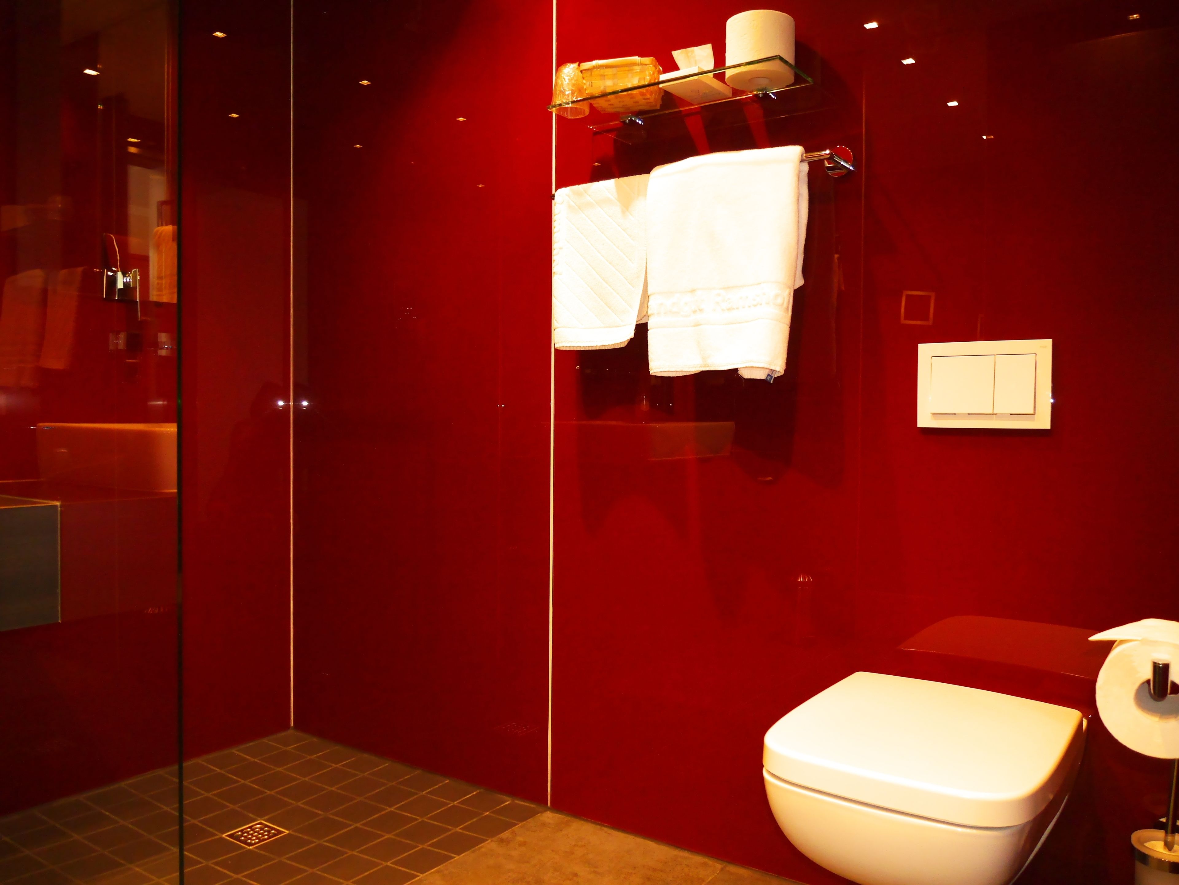 A bathroom with a red wall, a white toilet, and a glass shower enclosure.