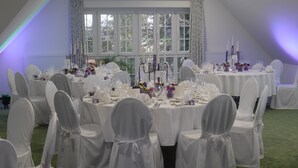 A banquet hall with round tables set for a formal event, white chairs with ties, and a large window with curtains. - Landgut Ramshof (Willich)