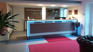 Un área de recepción con mostrador, planta y alfombra roja.