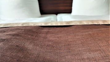 Una cama con almohadas blancas y una colcha marrón con textura. Una tarjeta de bienvenida con globos está sobre la cama.