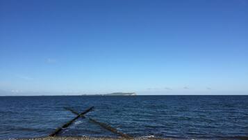 A beach with a clear sky, calm sea, and a distant island.