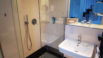 Un baño moderno con ducha envuelta en vidrio, un lavabo blanco y un espejo sobre él.