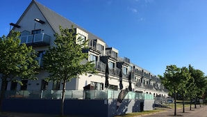 Un edificio moderno con varios balcones y ventanas amplias, rodeado de árboles y un cielo azul despejado.