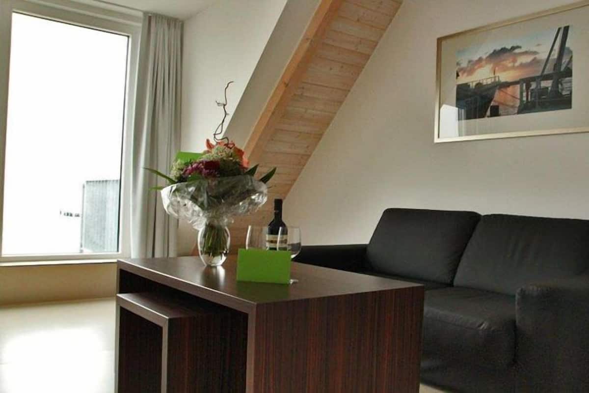 A modern living room with a dark brown wooden coffee table, a black sofa, and a framed picture on the wall.