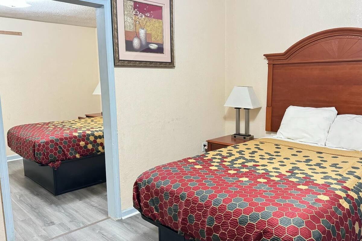 A hotel room with two beds, a wooden headboard, a nightstand with a lamp, and a framed picture on the wall.
