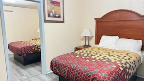 A hotel room with two beds, a wooden headboard, a nightstand with a lamp, and a framed picture on the wall.
