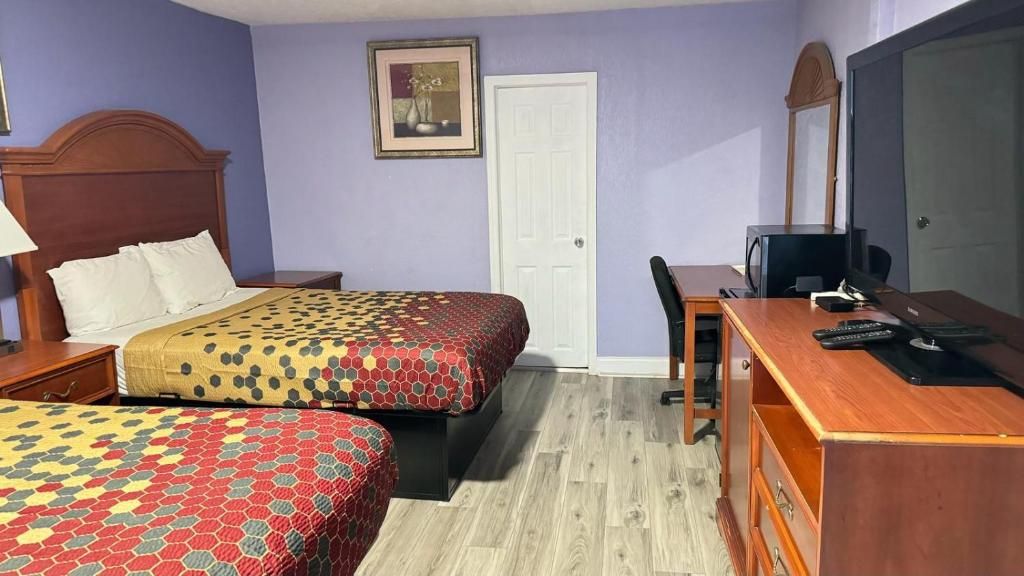 Quarto de hotel com duas camas, uma escrivaninha, uma cadeira, uma televisão e uma porta.
