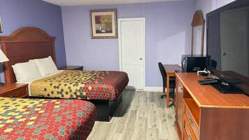 Quarto de hotel com duas camas, uma escrivaninha, uma cadeira, uma televisão e uma porta.
