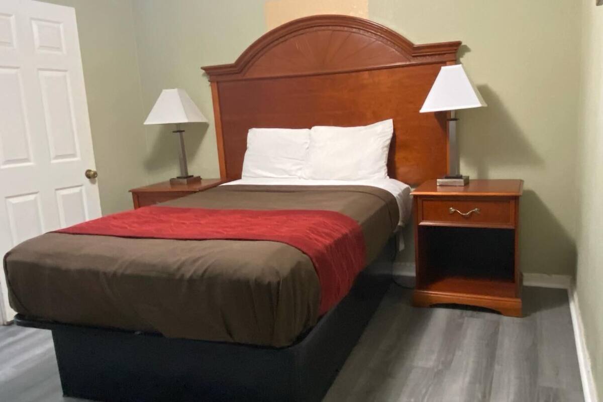 A neatly made bed with a red blanket, two bedside tables with lamps, and a wooden headboard.