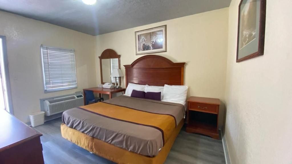 Una habitación de hotel con una cama, mesitas de noche, un espejo, una ventana con persianas y un radiador.
