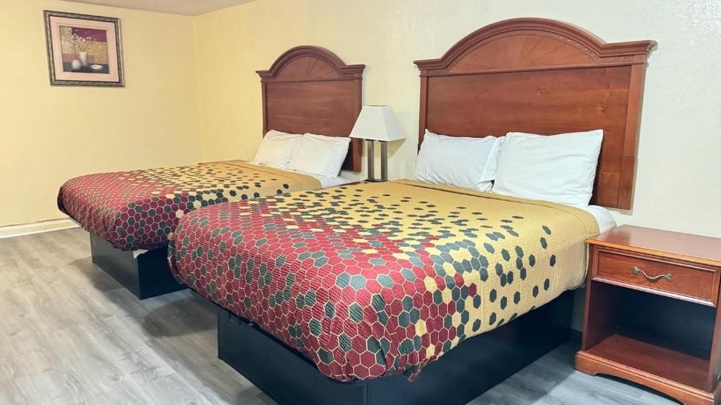 A hotel room with two beds, each with a wooden headboard, a bedside table, and a lamp.