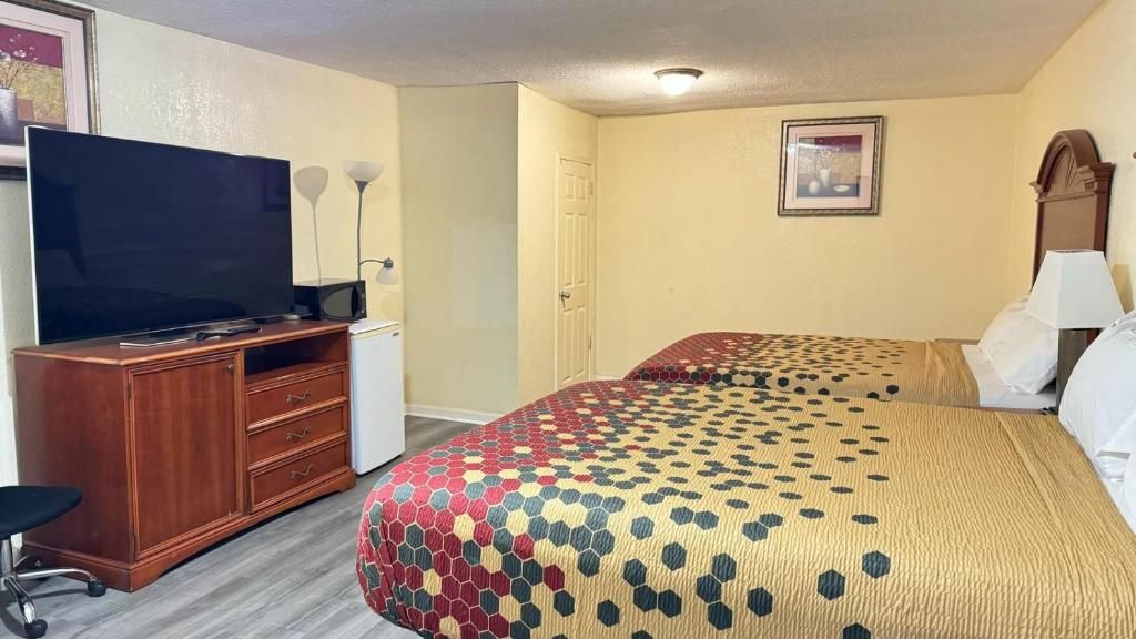 A hotel room with a television, a desk, two beds with patterned bedding, and a door.